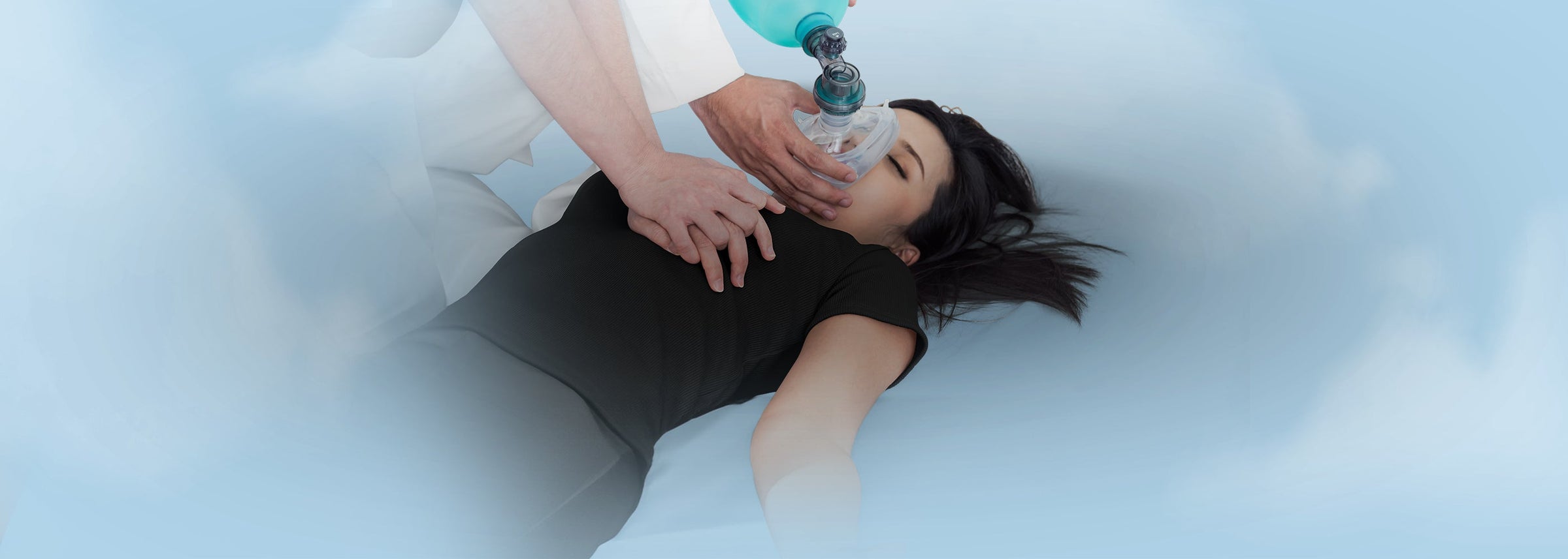 Medical professional administering CPR to a patient using a rescue mask and manual resuscitator, illustrating emergency airway management supplies and face shields.