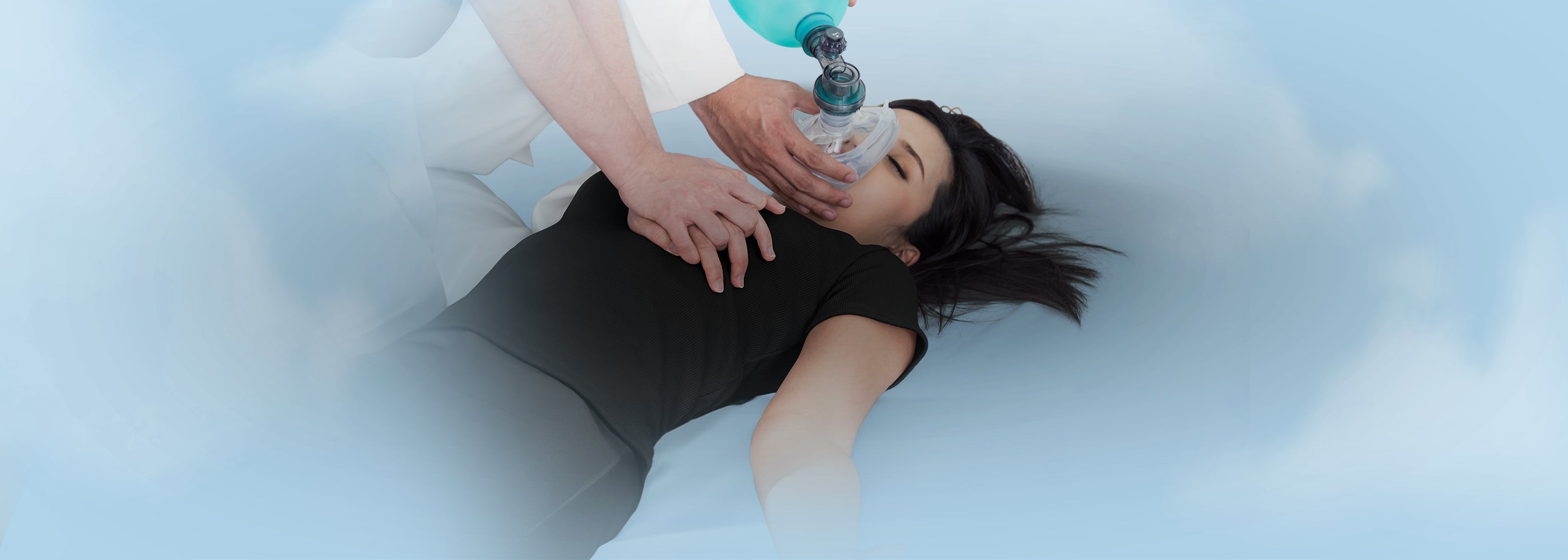 Medical professional administering CPR to a patient using a rescue mask and manual resuscitator, illustrating emergency airway management supplies and face shields.