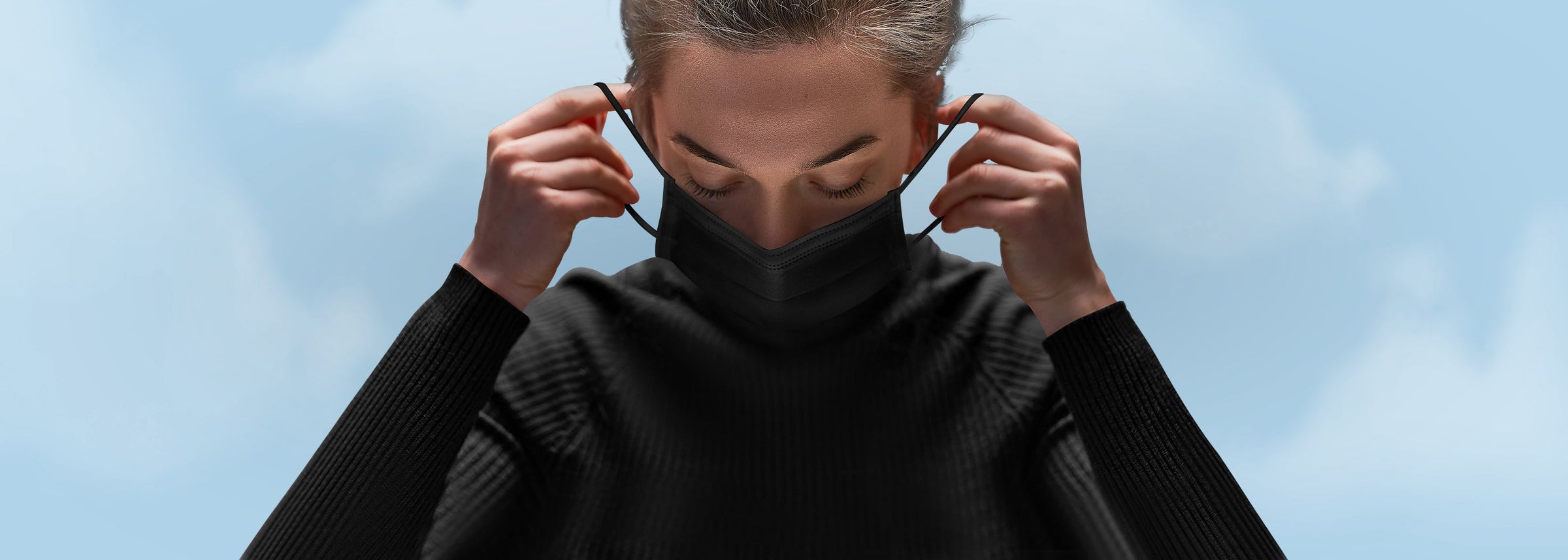 A person wearing a black disposable medical face mask on a light blue background, representing the PPE & Face Masks collection.