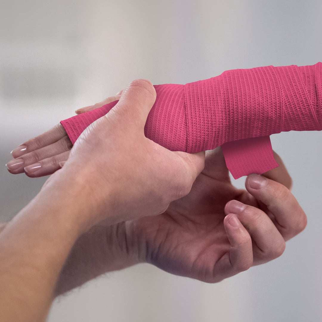 Person applying white bandage to a wrist against a plain background