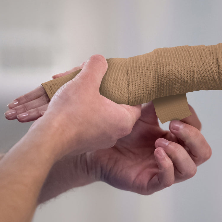 Person applying white bandage to a wrist against a plain background