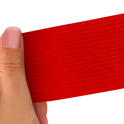 Hand holding a Red strip of adhesive bandage wrap with a textured pattern on a white background