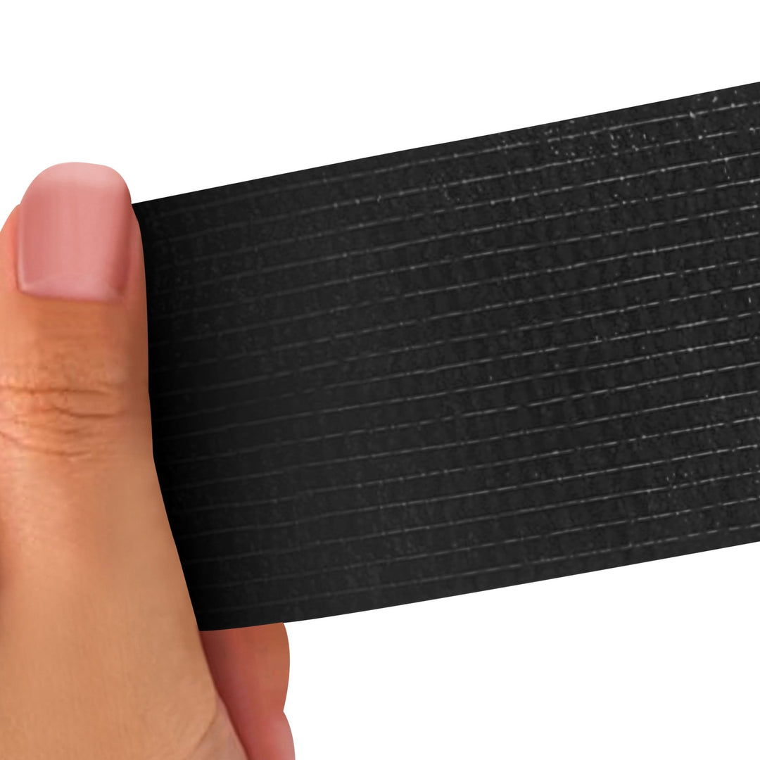Hand holding a Black strip of adhesive bandage wrap with a textured pattern on a white background