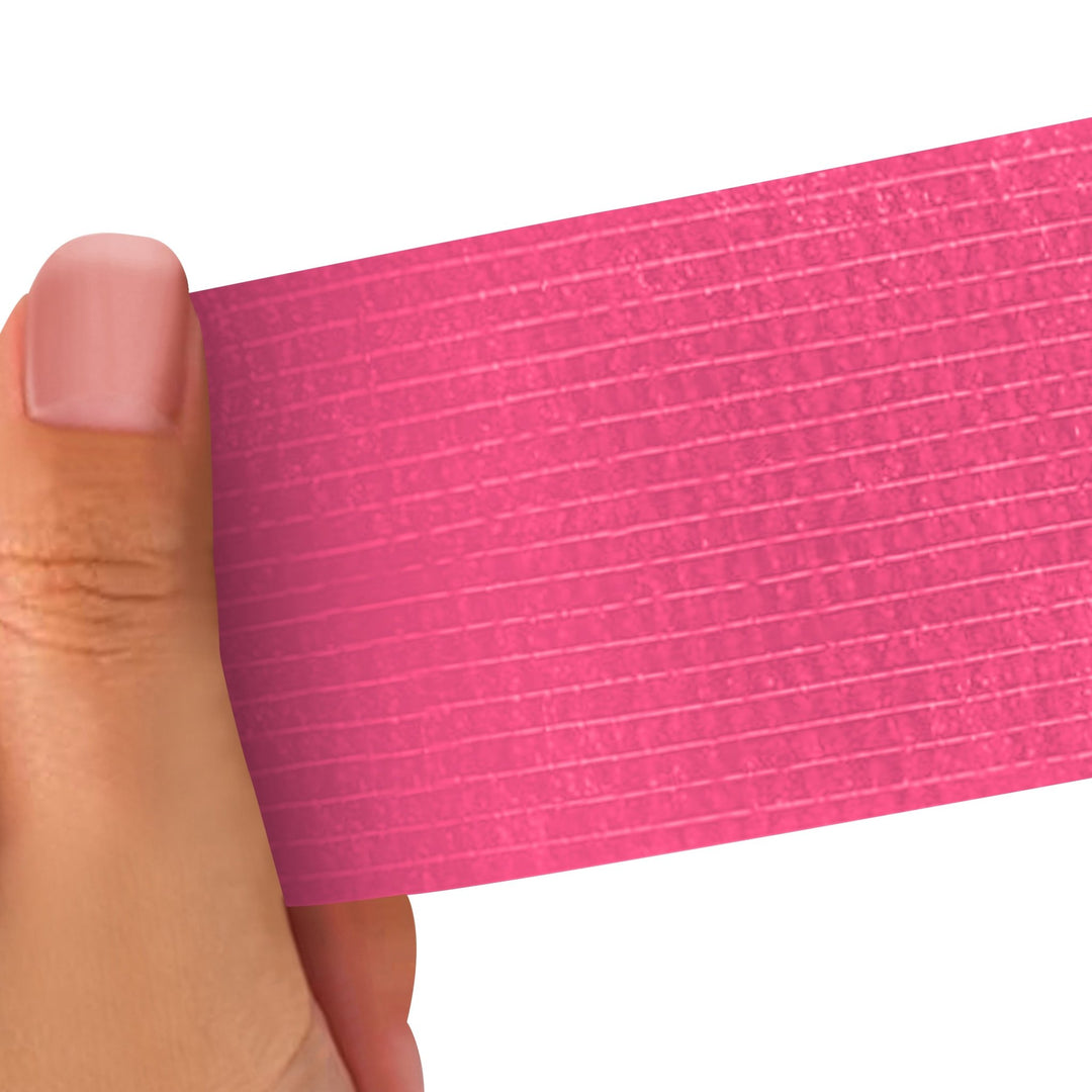 Hand holding a Pink strip of adhesive bandage wrap with a textured pattern on a white background