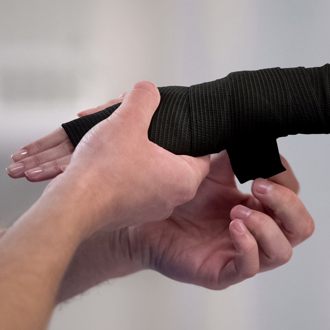 Person applying white bandage to a wrist against a plain background