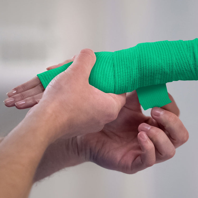 Person applying white bandage to a wrist against a plain background