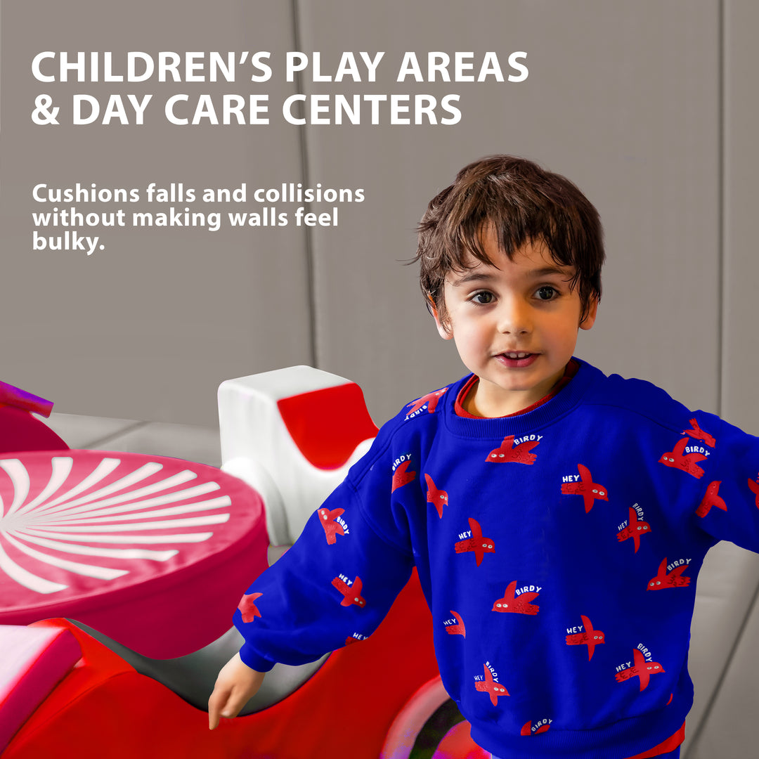 A young boy playing in a colorful indoor area with the walls lined with gray safety padding, featuring text that suggests use for "CHILDREN'S PLAY AREAS & DAY CARE CENTERS" to cushion falls.