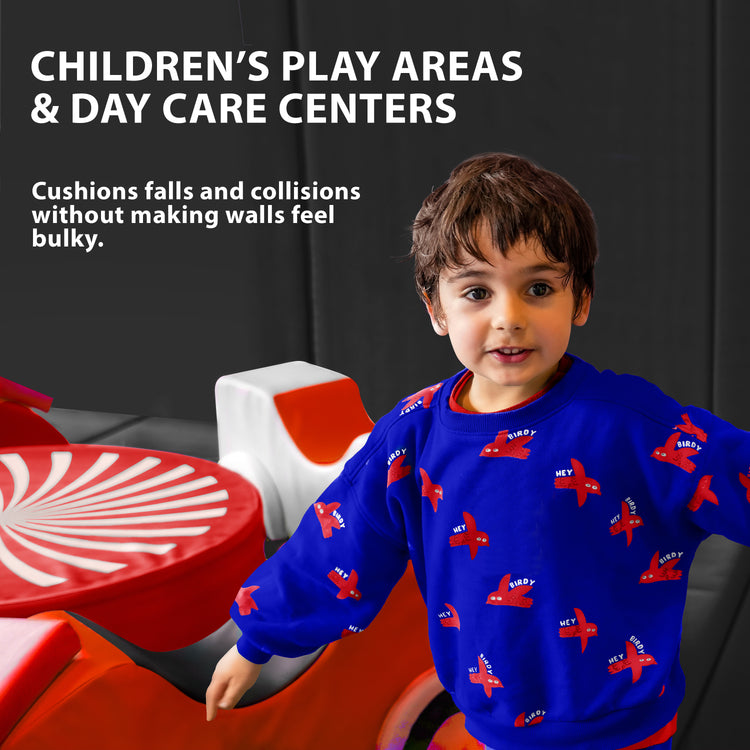 A young boy playing in a colorful indoor area with the walls lined with blue safety padding, featuring text that suggests use for "CHILDREN'S PLAY AREAS & DAY CARE CENTERS" to cushion falls.