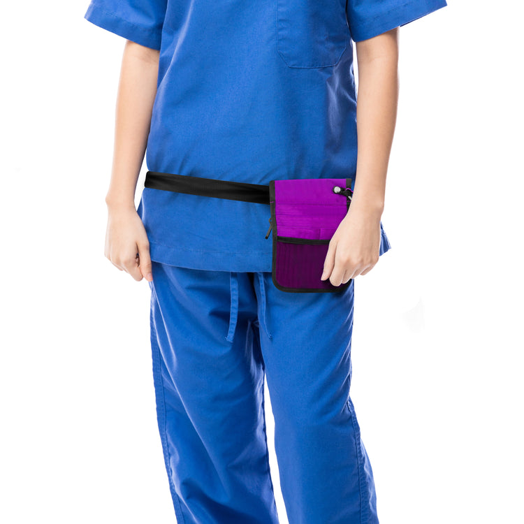 A cropped lifestyle shot focusing on the utility of the bag. A nurse in blue scrubs is shown from the torso down, wearing the purple medical organizer belt around her hips. The bag sits flat against the body, demonstrating its slim profile.