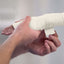 Person applying white bandage to a wrist against a plain background