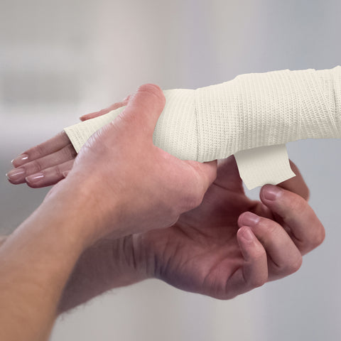 Person applying white bandage to a wrist against a plain background