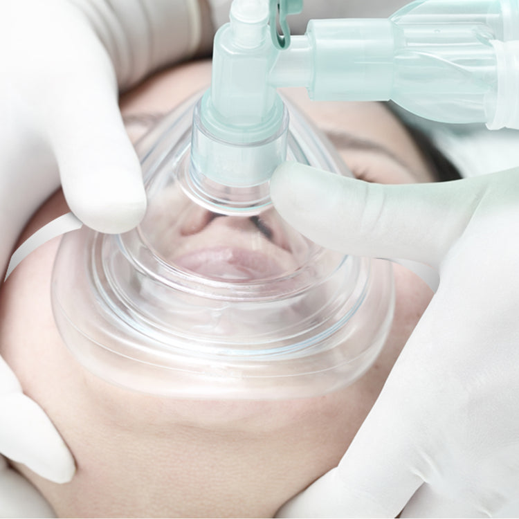 A medical simulation showing a clear CPR mask placed over a patient's nose and mouth, securely held by gloved hands while connected to a manual resuscitation bag.