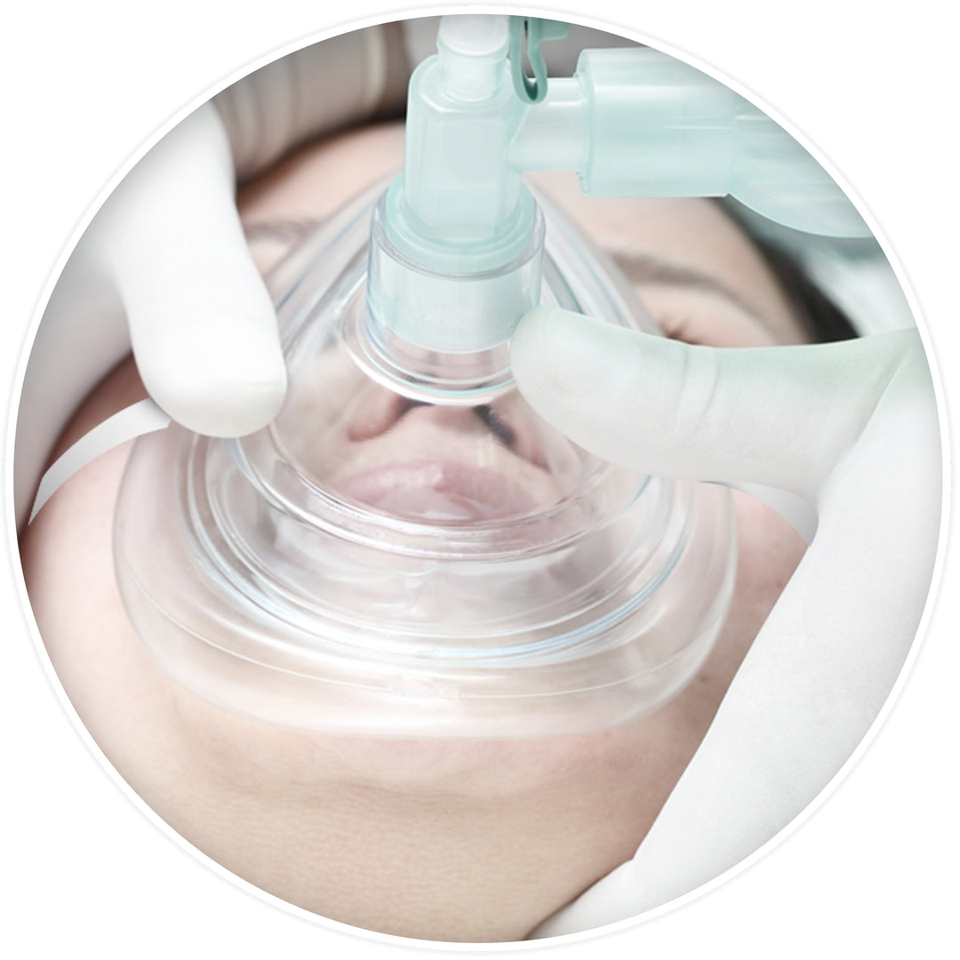 A medical simulation showing a clear CPR mask placed over a patient's nose and mouth, securely held by gloved hands while connected to a manual resuscitation bag.