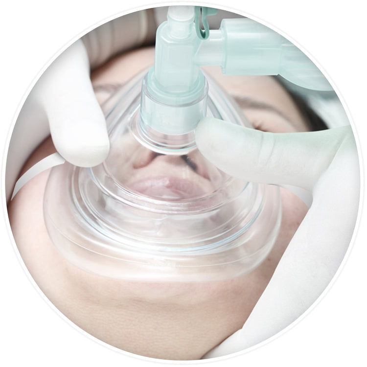 A medical simulation showing a clear CPR mask placed over a patient's nose and mouth, securely held by gloved hands while connected to a manual resuscitation bag.