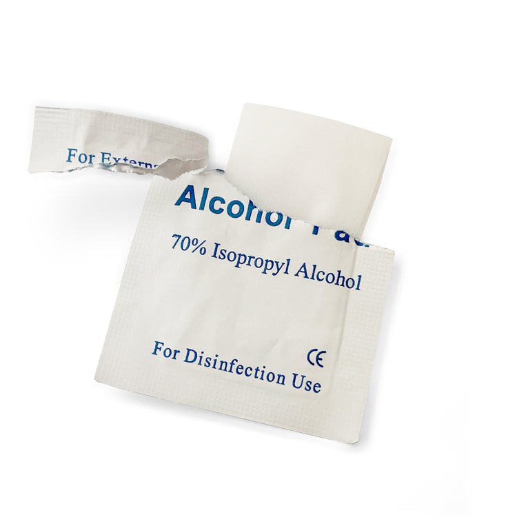 A close-up of a white, torn-open packet labeled "Alcohol Pad" containing a 70% Isopropyl Alcohol wipe for disinfection, revealing the folded white pad inside.
