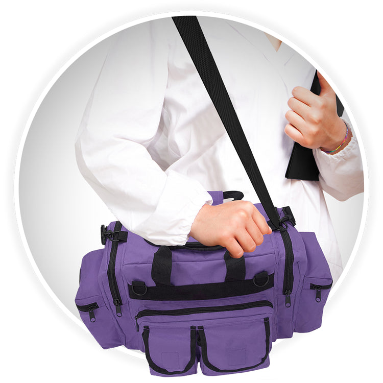 A close-up of a person wearing a white medical coat carrying the purple trauma bag. The bag is slung over their shoulder using the black adjustable strap, and their hand rests on the top handle.