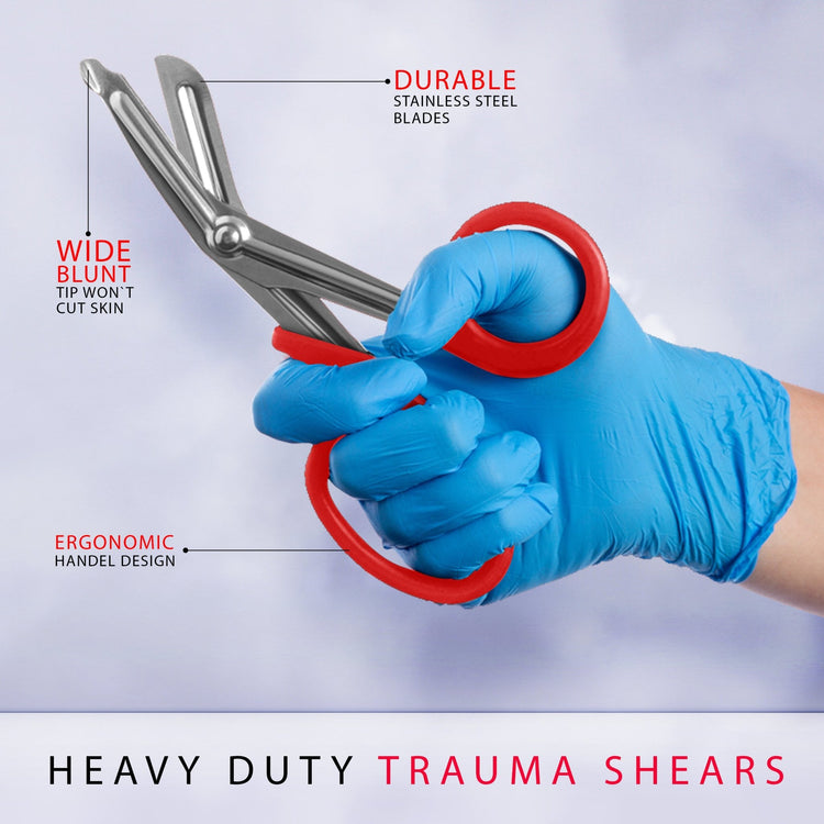 A gloved hand holding a pair of red heavy-duty trauma shears, highlighting the ergonomic handle and wide blunt tip designed to cut clothing safely without injuring skin.