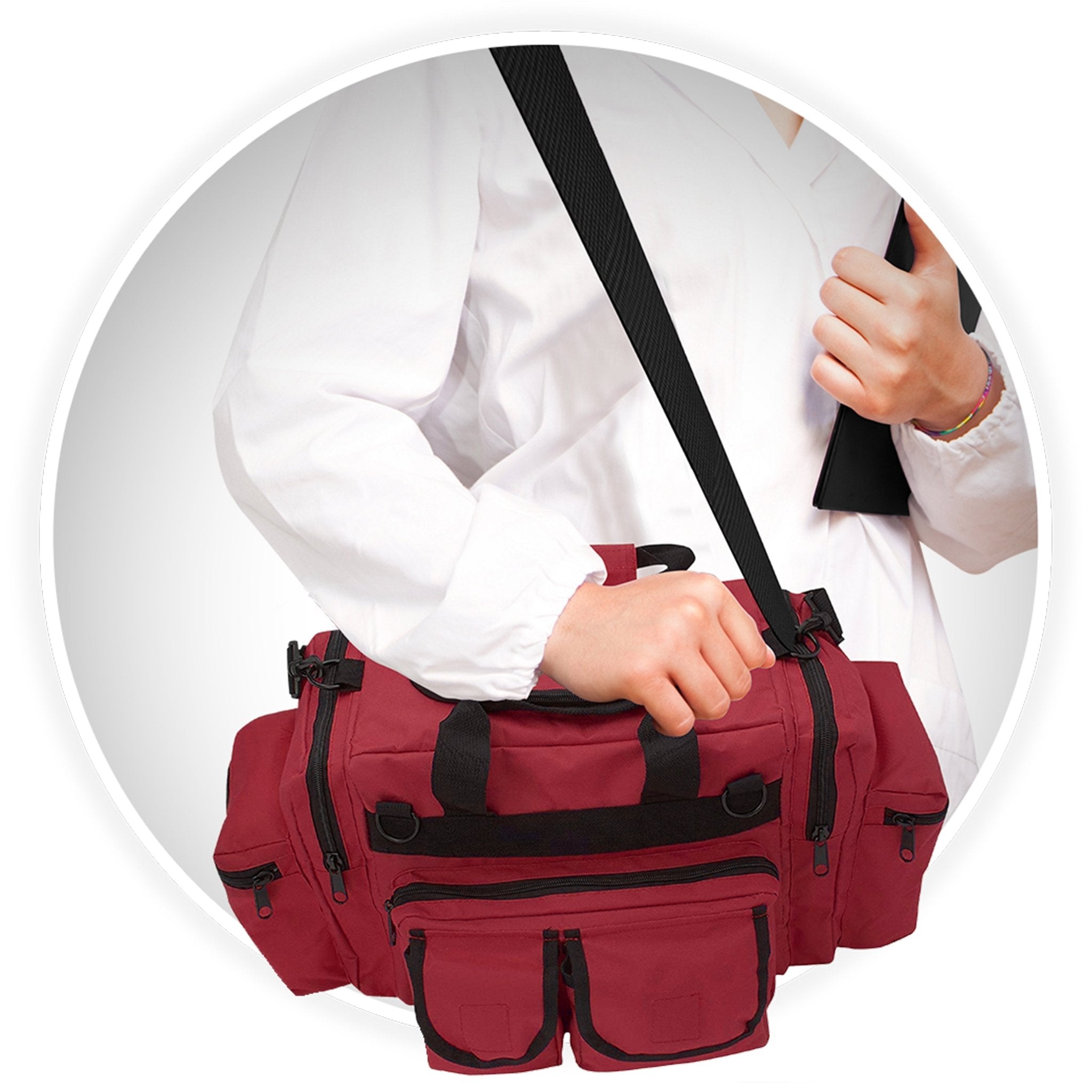 A close-up of a person wearing a white medical coat carrying the red trauma bag. The bag is slung over their shoulder using the black adjustable strap, and their hand rests on the top handle.