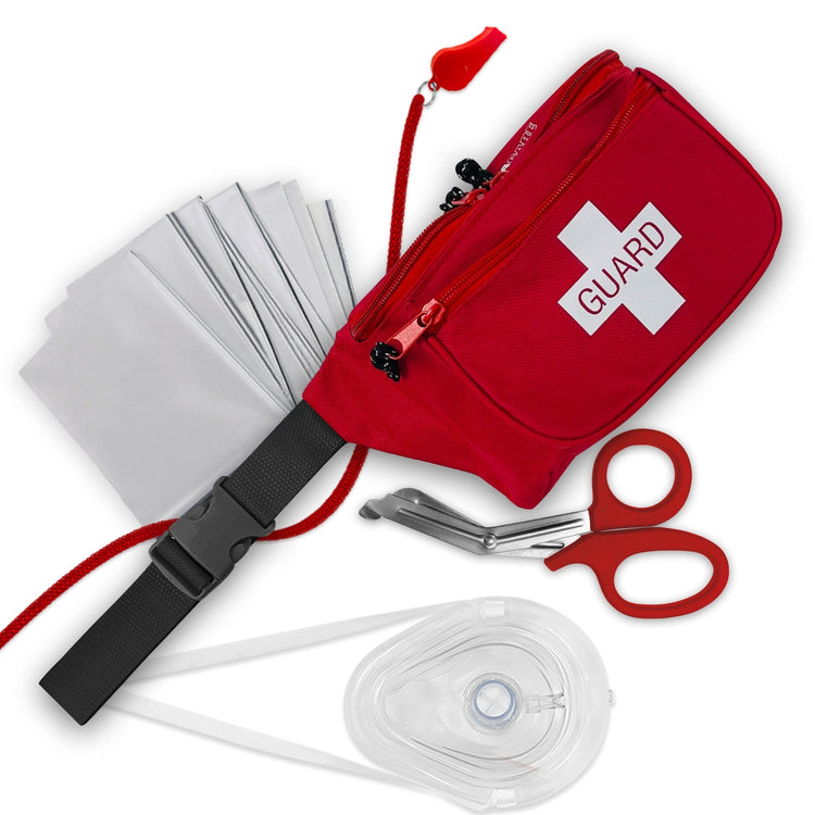 A flat lay display of a lifeguard kit. The items include a red fanny pack with "GUARD" printed on a white cross, a red whistle on a lanyard, silver trauma shears, a clear CPR mask, and a folded silver emergency blanket.