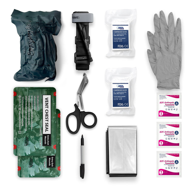 A flat-lay photograph of the emergency kit contents arranged neatly on a white background. Items include a packaged Israeli bandage, a black combat tourniquet, two packages of compressed gauze, a pair of gray disposable gloves, two green packages of vent chest seals, black-handled trauma shears, a silver folded emergency blanket, three small antiseptic wipe packets, and a black marker.