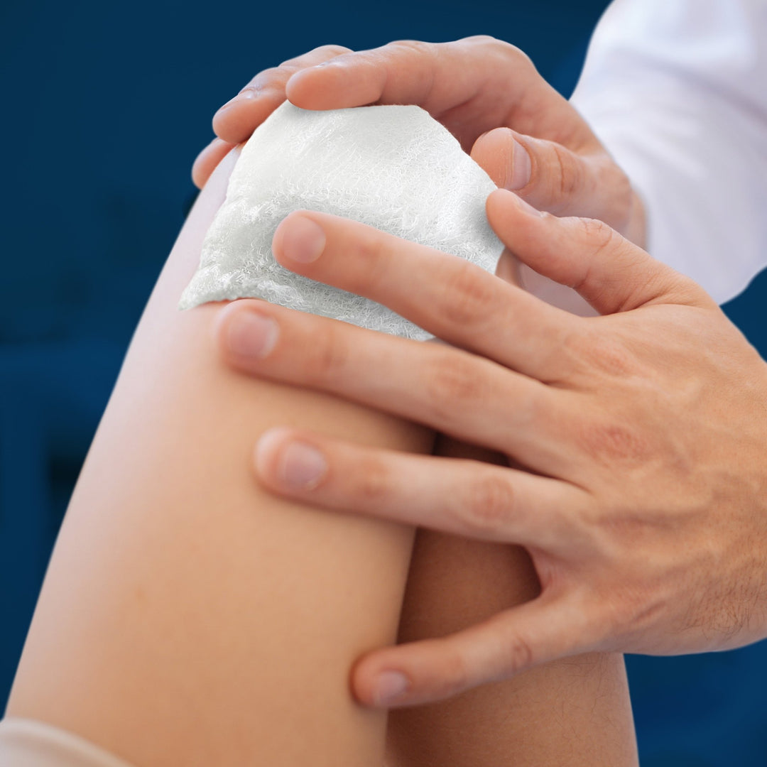 A demonstration of the gauze in use, showing a person applying the white absorbent material to a patient's knee or lower leg to cover an injury.