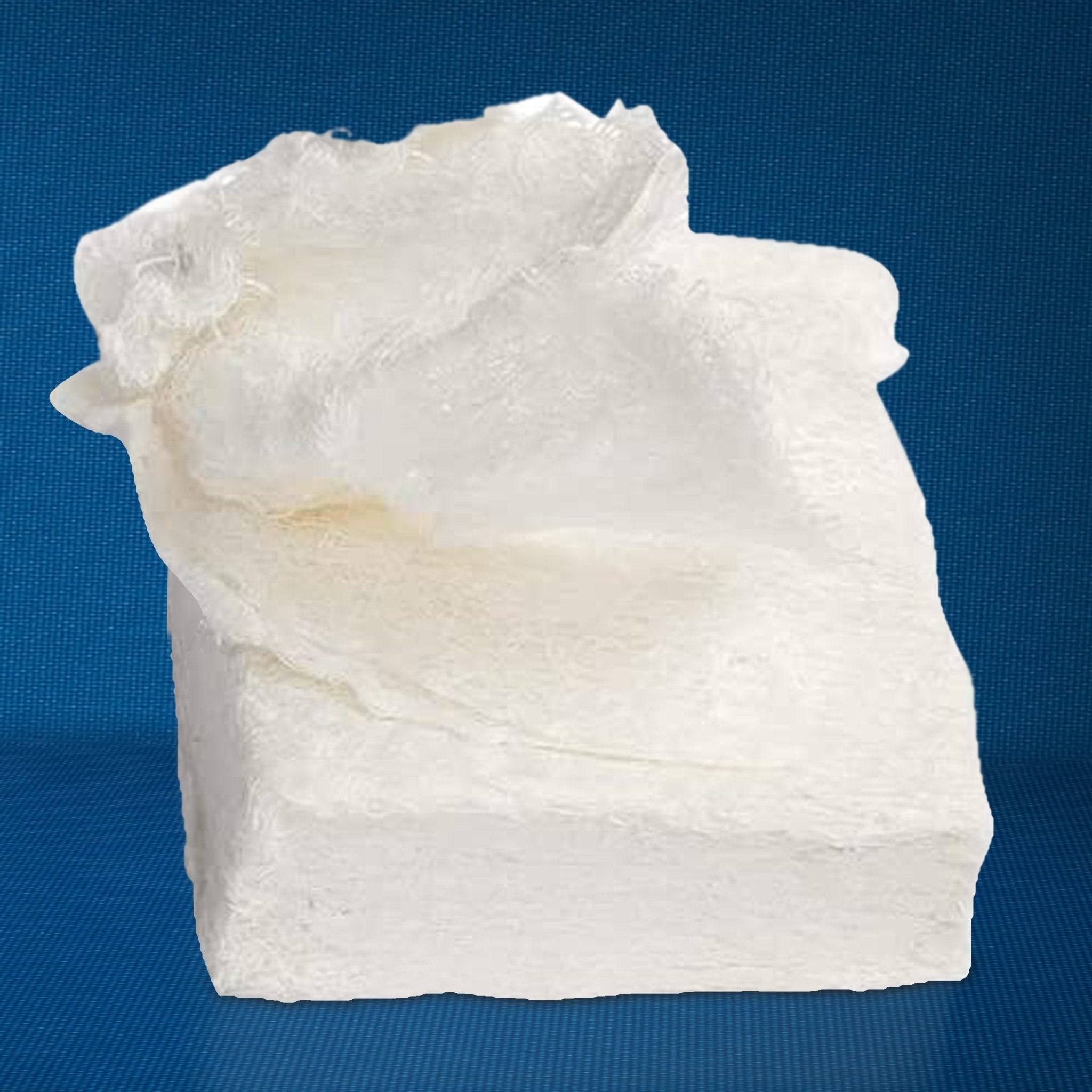 A close-up view of a rectangular block of white crinkle-cut gauze after being removed from its packaging. The image highlights the dense, compressed texture of the cotton material before it is unfolded.