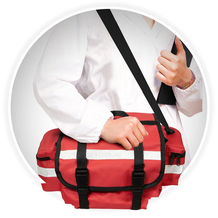 A close-up of a medical professional wearing a white coat, carrying the red bag. They are holding the top handle with one hand while the adjustable black shoulder strap rests across their body.