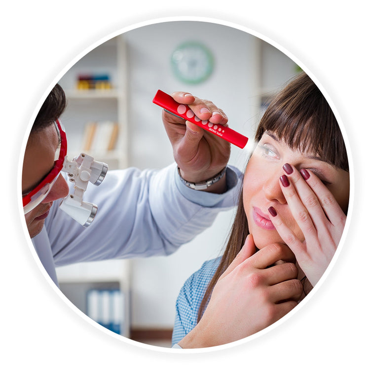 A circular frame showing a medical professional wearing magnifying loupes using the red pen light to examine a female patient's eye while she covers her other eye with her hand.