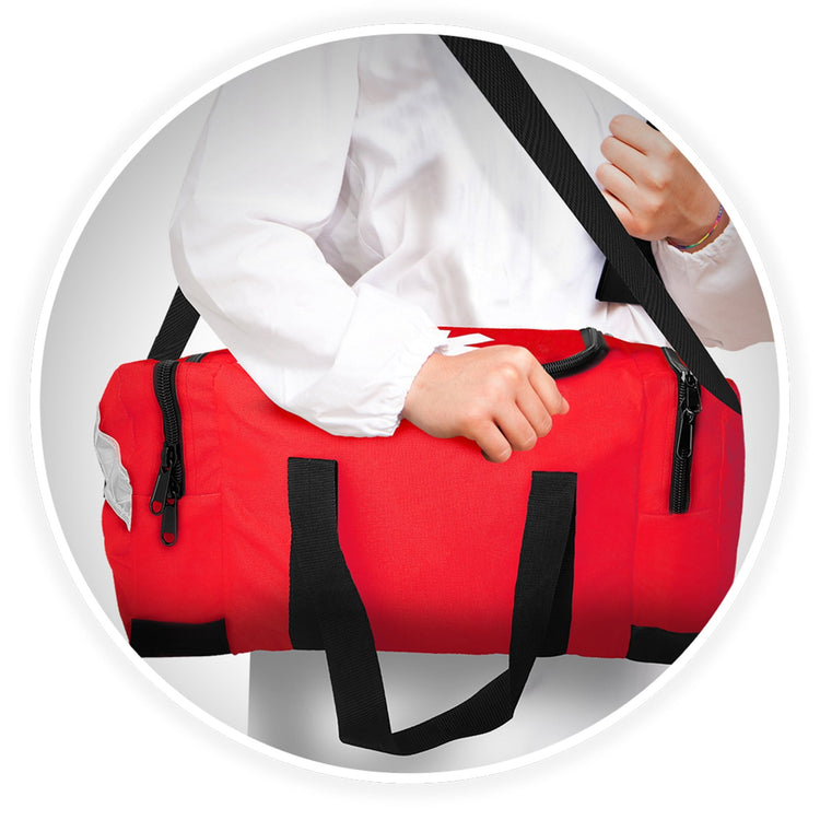 A person wearing a white medical coat carries the red trauma bag over their shoulder using the adjustable black strap.