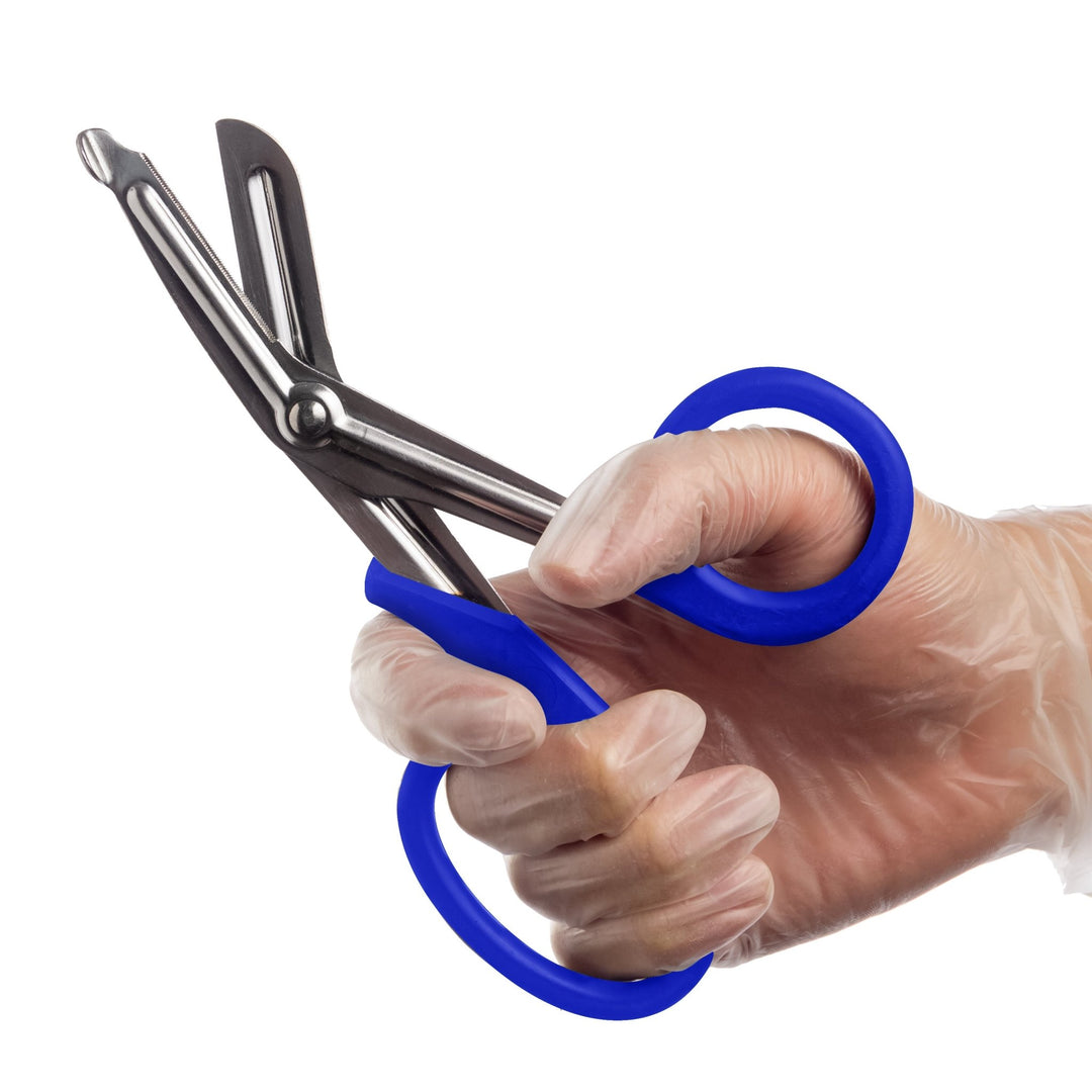 A hand wearing a clear medical glove holds a pair of open trauma shears with royal blue handles against a white background.