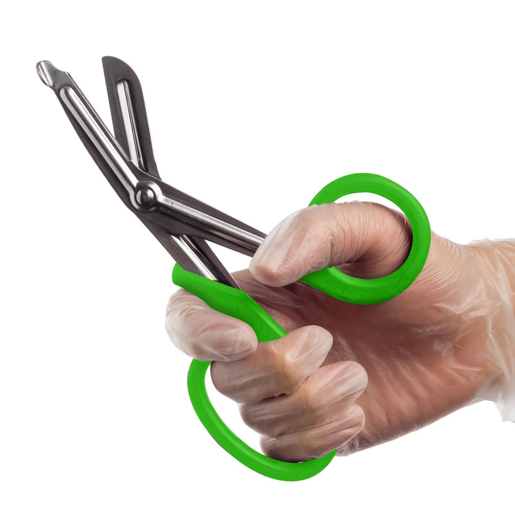 A hand wearing a clear medical glove holds a pair of open trauma shears with green handles against a white background.