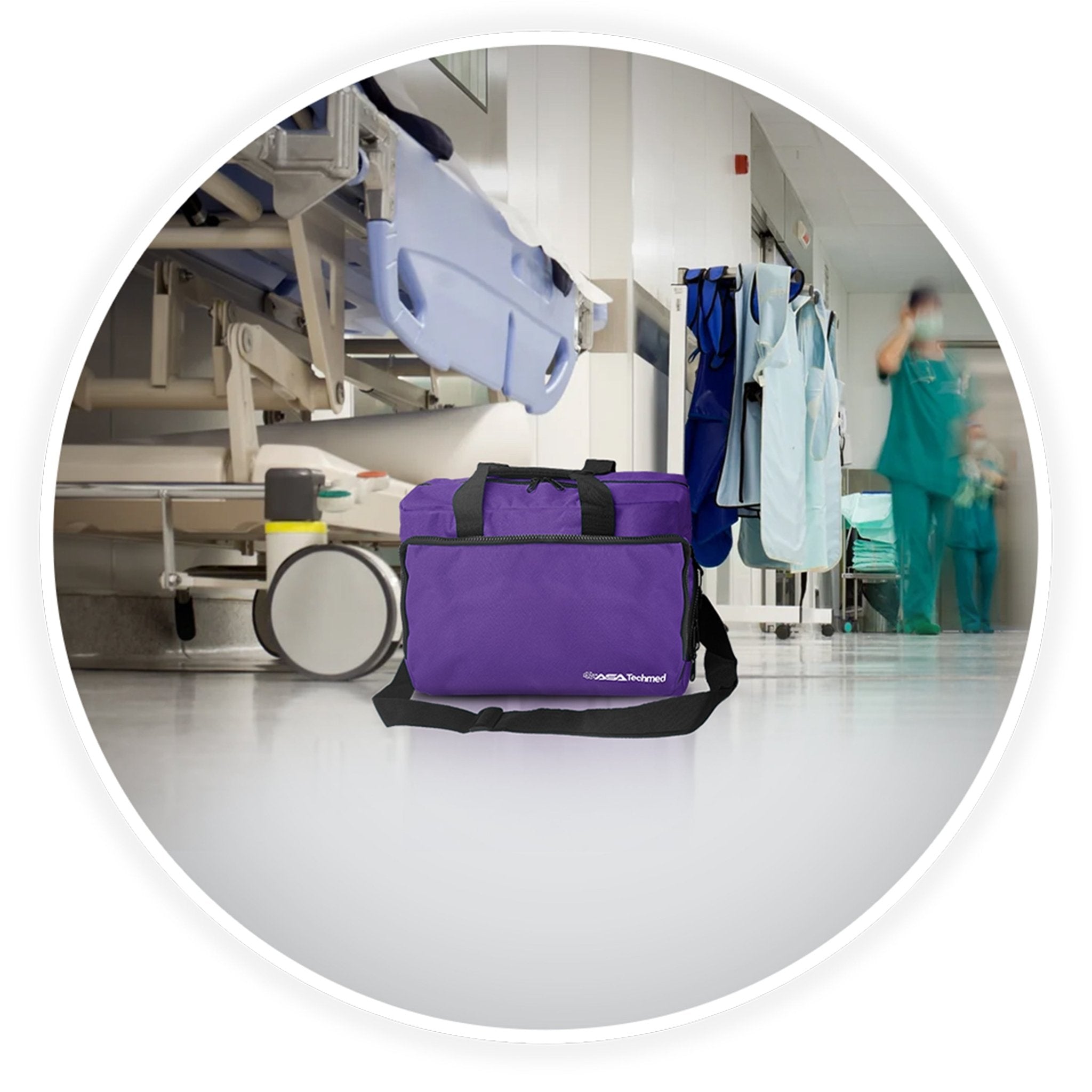 A contextual image showing the purple trauma bag sitting on the floor of a clean hospital hallway, with a medical gurney and blurred healthcare staff in the background.
