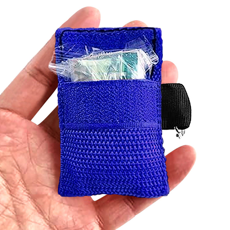 A hand holding an open blue CPR face shield keychain pouch, revealing a clear plastic packet containing a face shield and gloves stored inside the front velcro pocket.