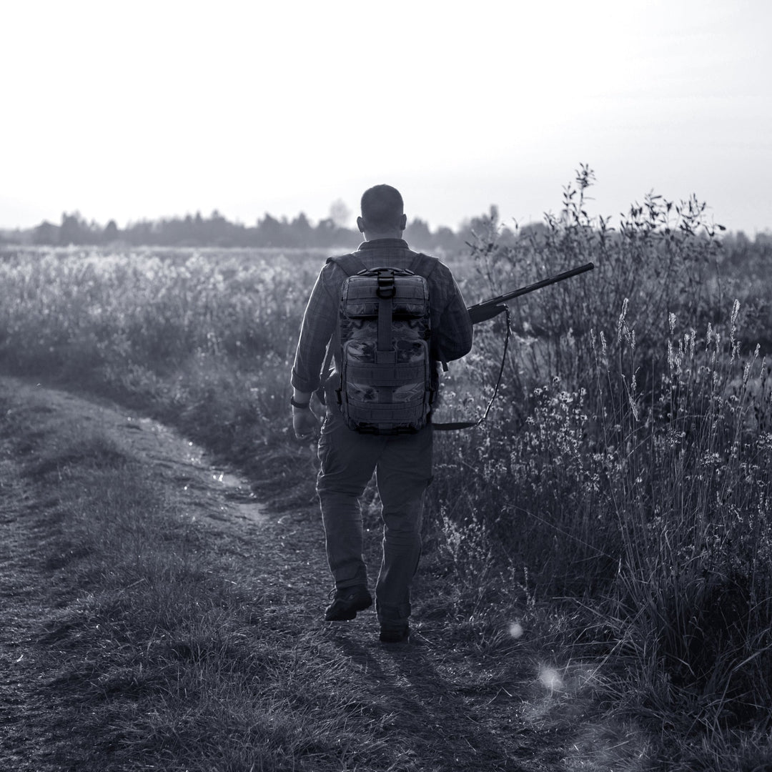 A man carrying the tactical backpack while walking through a field, illustrating its suitability for hiking, travel, and outdoor activities.