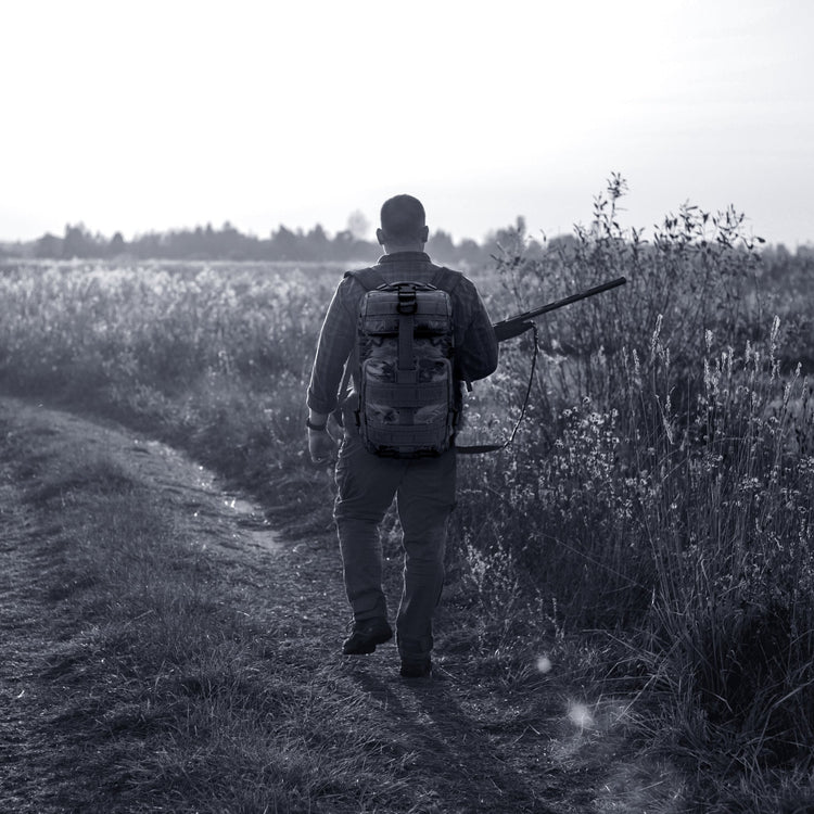 A man carrying the tactical backpack while walking through a field, illustrating its suitability for hiking, travel, and outdoor activities.
