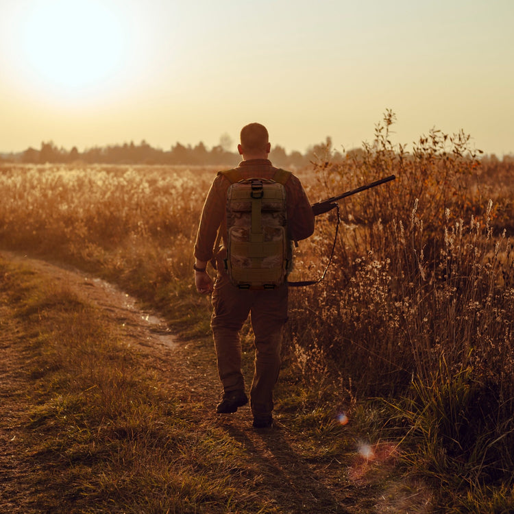A man carrying the tactical backpack while walking through a field, illustrating its suitability for hiking, travel, and outdoor activities.