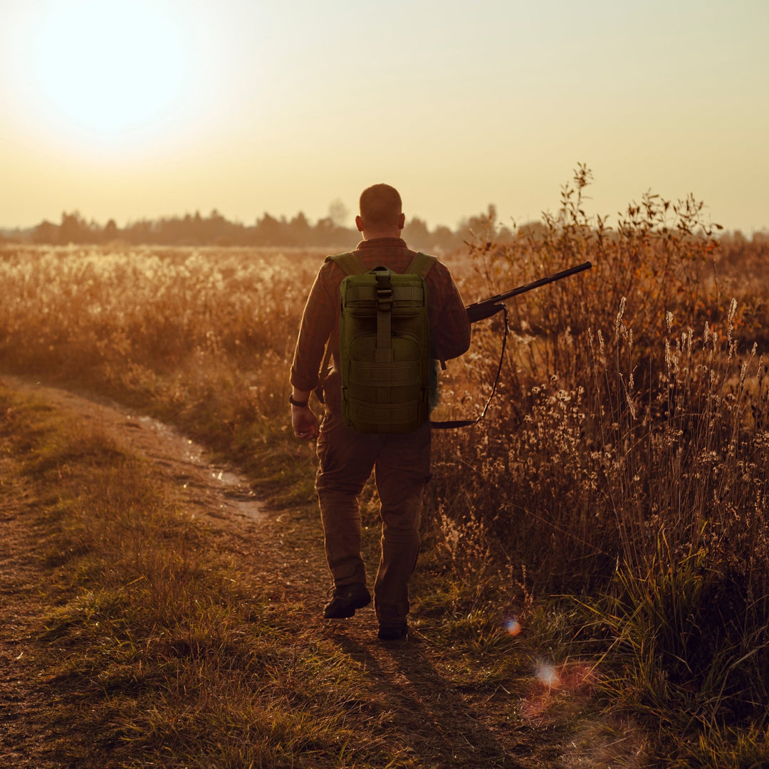 A man carrying the tactical backpack while walking through a field, illustrating its suitability for hiking, travel, and outdoor activities.