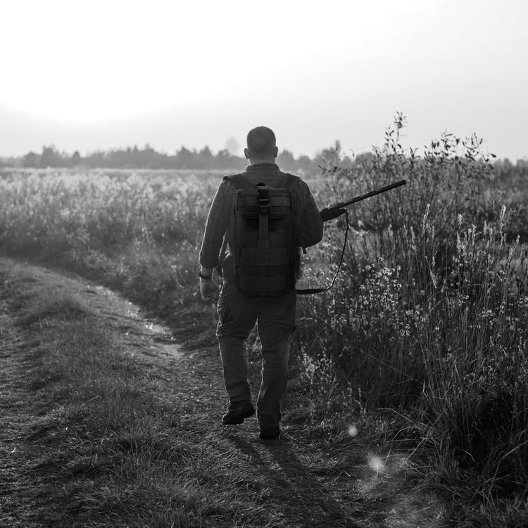 A man carrying the tactical backpack while walking through a field, illustrating its suitability for hiking, travel, and outdoor activities.