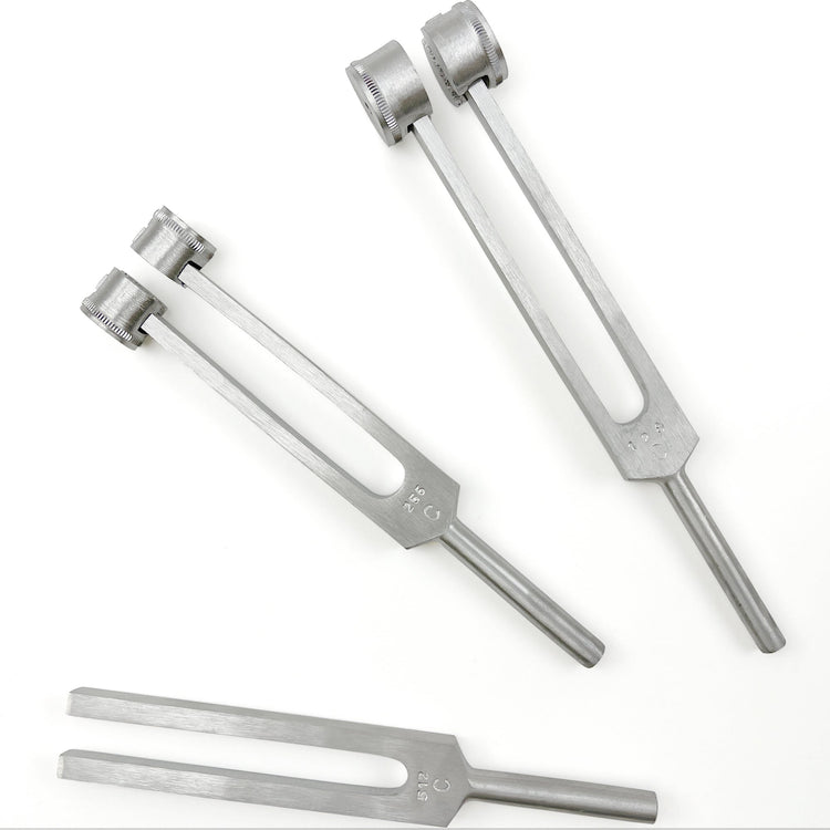 A top-down view of three silver aluminum tuning forks arranged on a white surface. The set includes a non-weighted C512 fork, a weighted C256 fork, and a weighted C128 fork, with their respective frequency markings engraved at the base of the prongs.