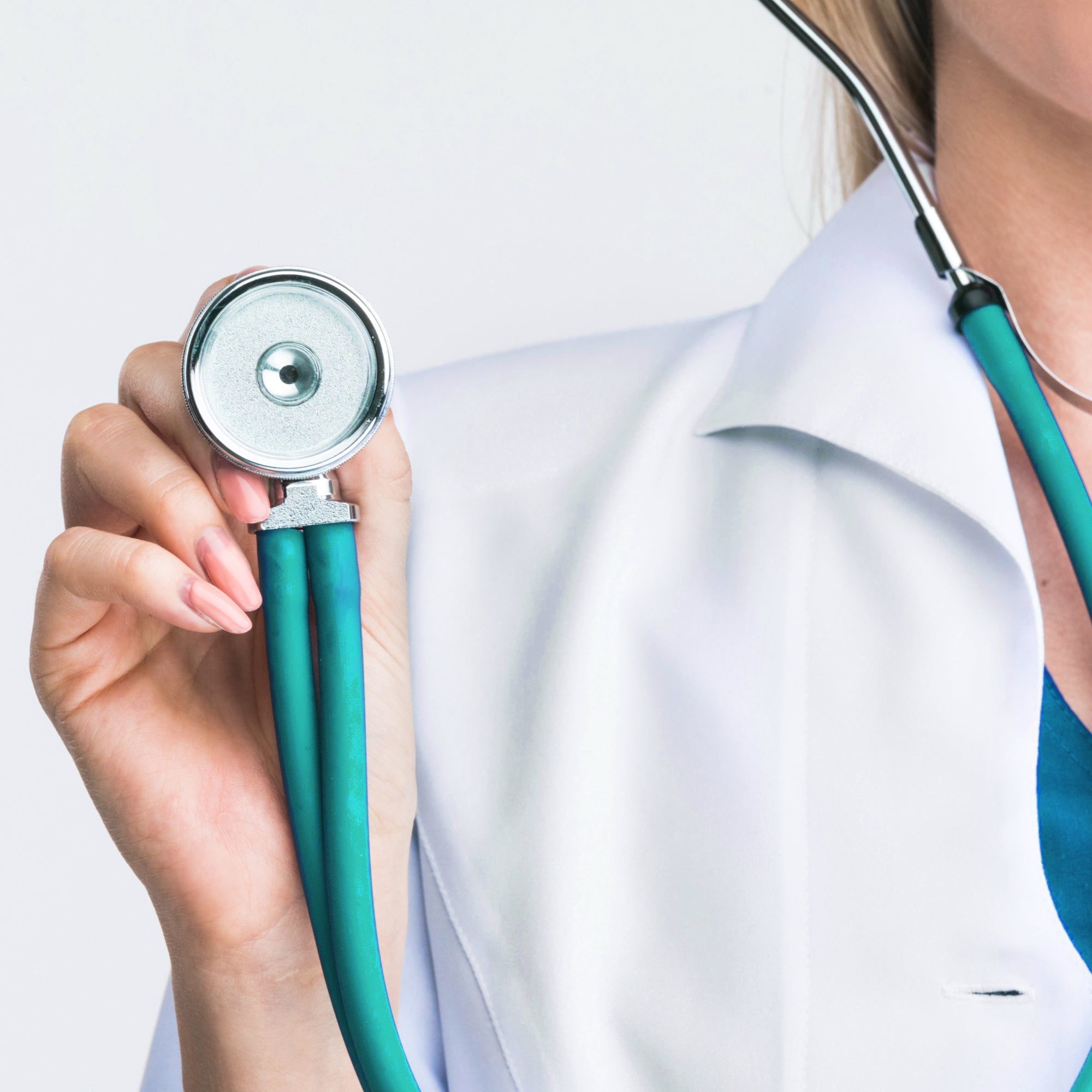 A lifestyle shot of a healthcare worker in a white lab coat holding the teal stethoscope’s chest piece forward as if ready to examine a patient.