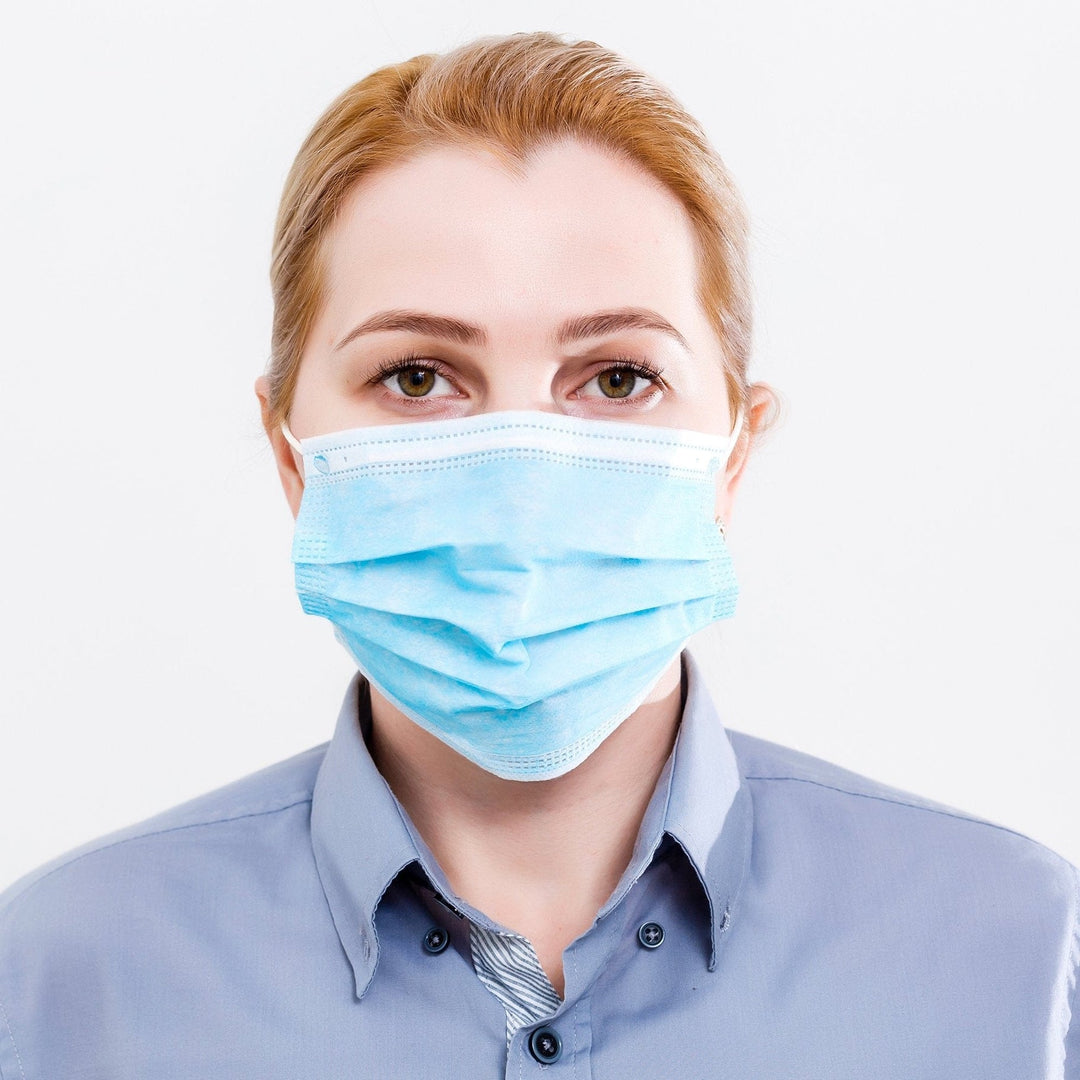 Portrait of a woman looking directly at the camera while wearing a blue professional-grade surgical mask to demonstrate proper facial coverage.