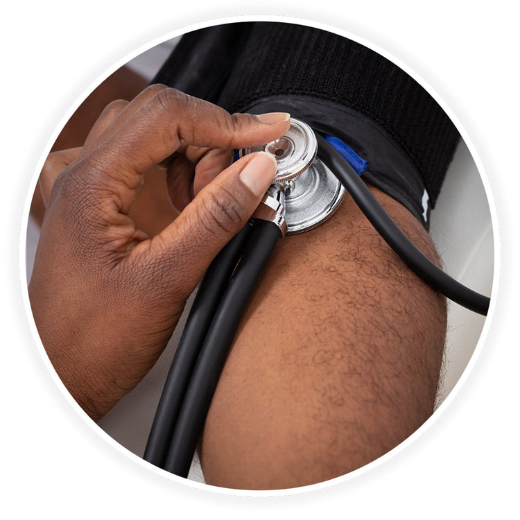A close-up photo demonstrating a medical examination. A dark-skinned healthcare professional's hand is shown using the black stethoscope to check a patient's blood pressure, placing the chest piece against the arm just below a black blood pressure cuff.