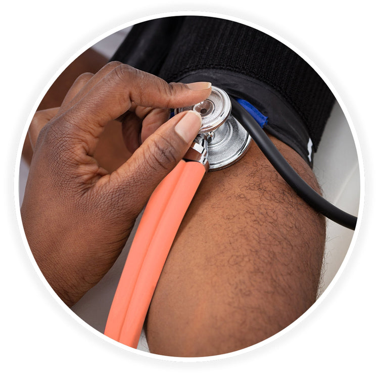 A close-up photo demonstrating a medical examination. A dark-skinned healthcare professional's hand is shown using the pink stethoscope to check a patient's blood pressure, placing the chest piece against the arm just below a black blood pressure cuff.