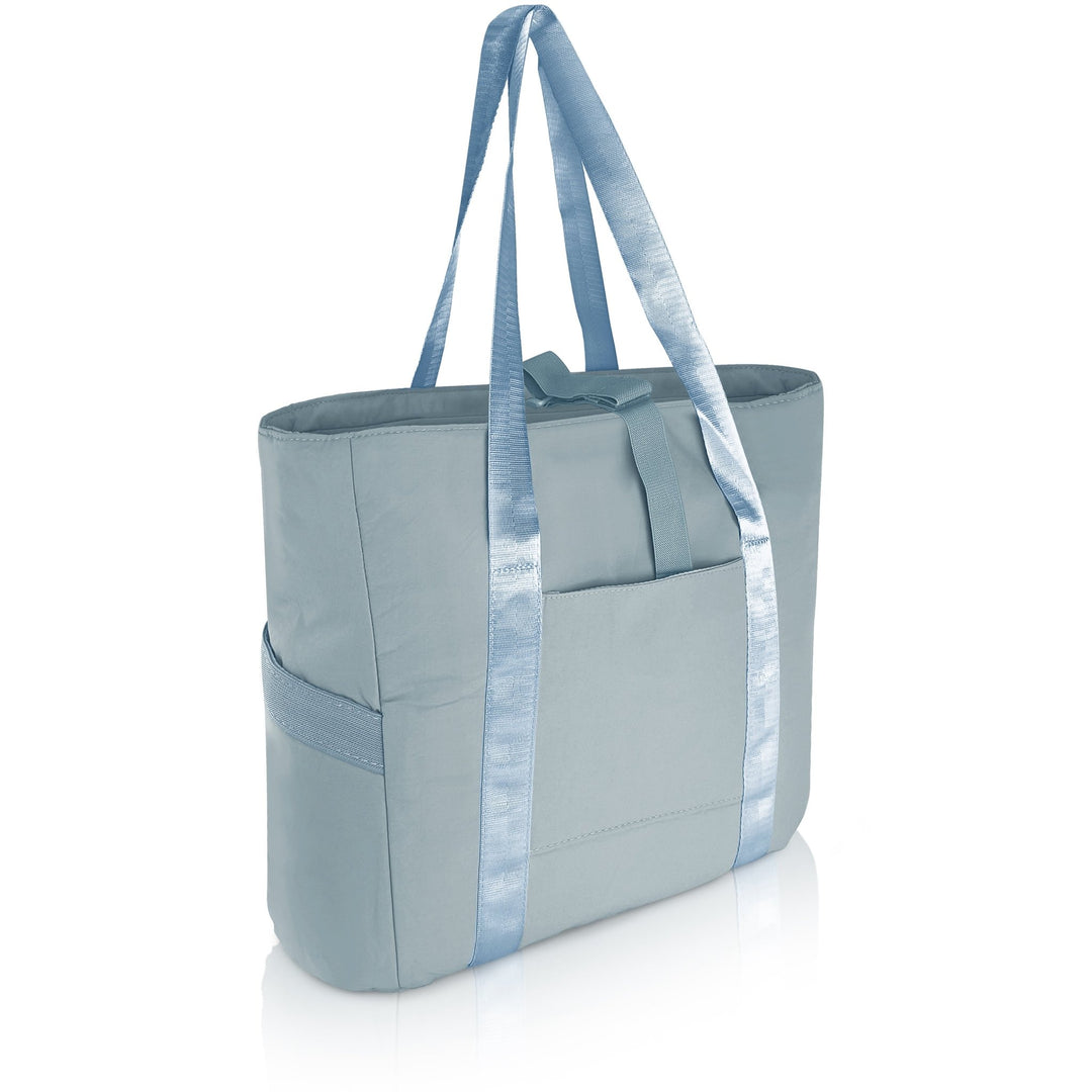 A 3/4 angle studio shot of the empty blue tote bag against a white background. The image displays the dual shoulder straps, the front slip pocket, and the side elastic pockets.